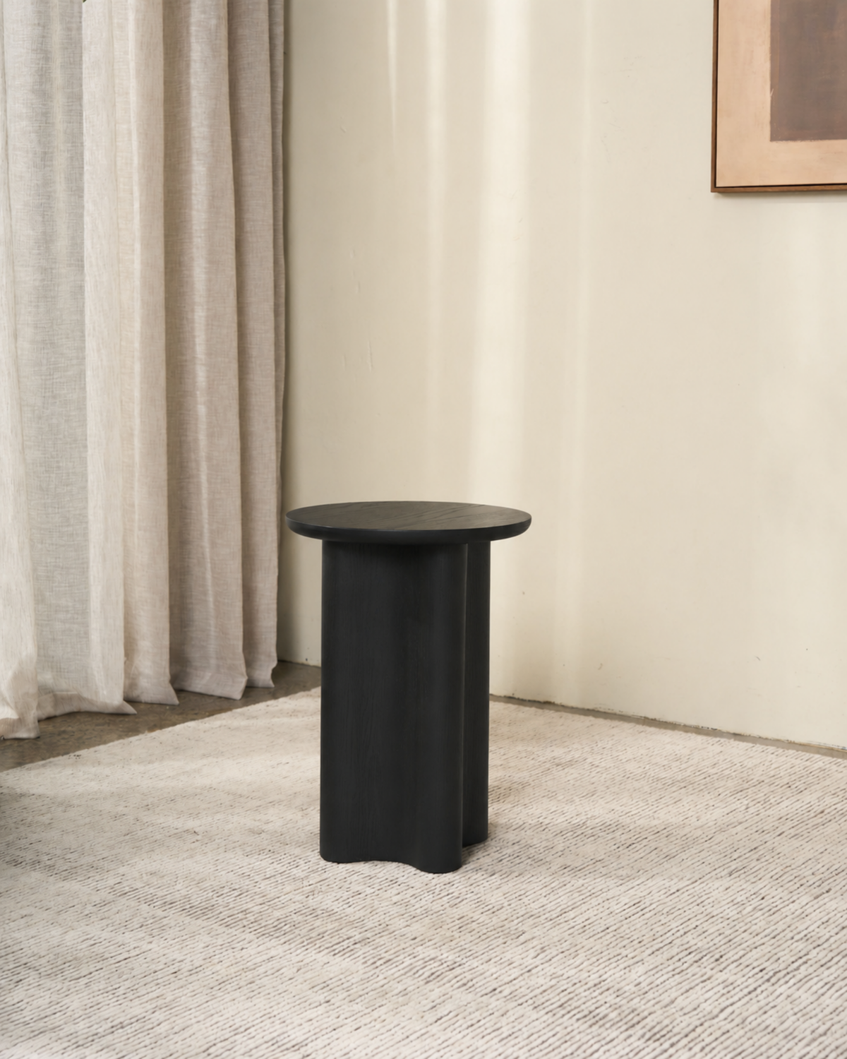 Luma Side Table shown in the Black Oak colour option on a pale rug in a corner by linen curtains
