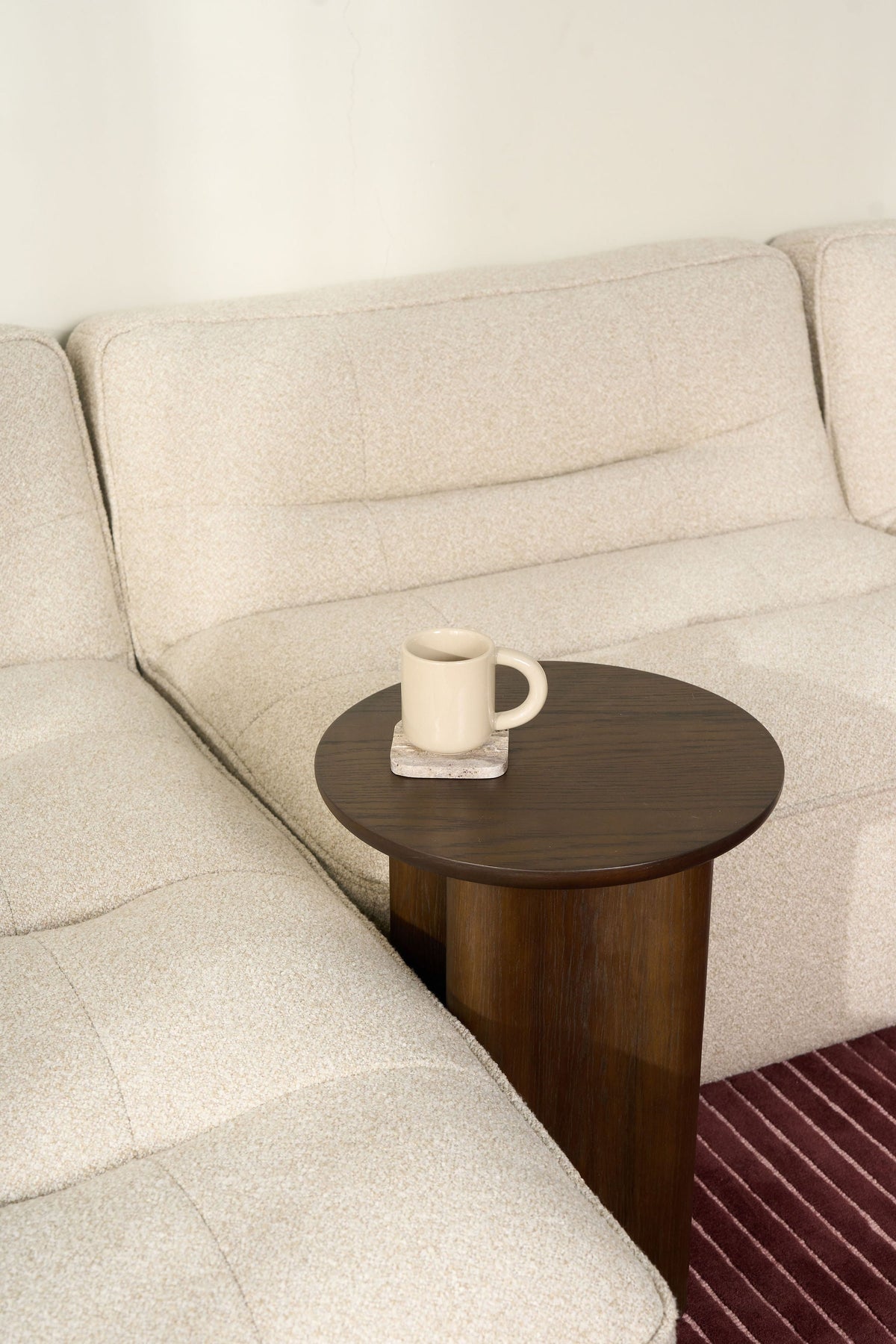 Brown Oak Luma Side Table pressed against a cream boucle sofa with a cream mug on a stone coaster