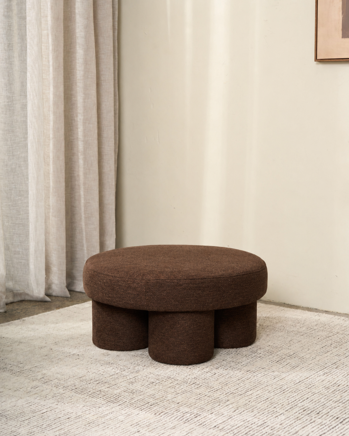 Round ottoman in a dark chocolate brown textured weave on a pale rug