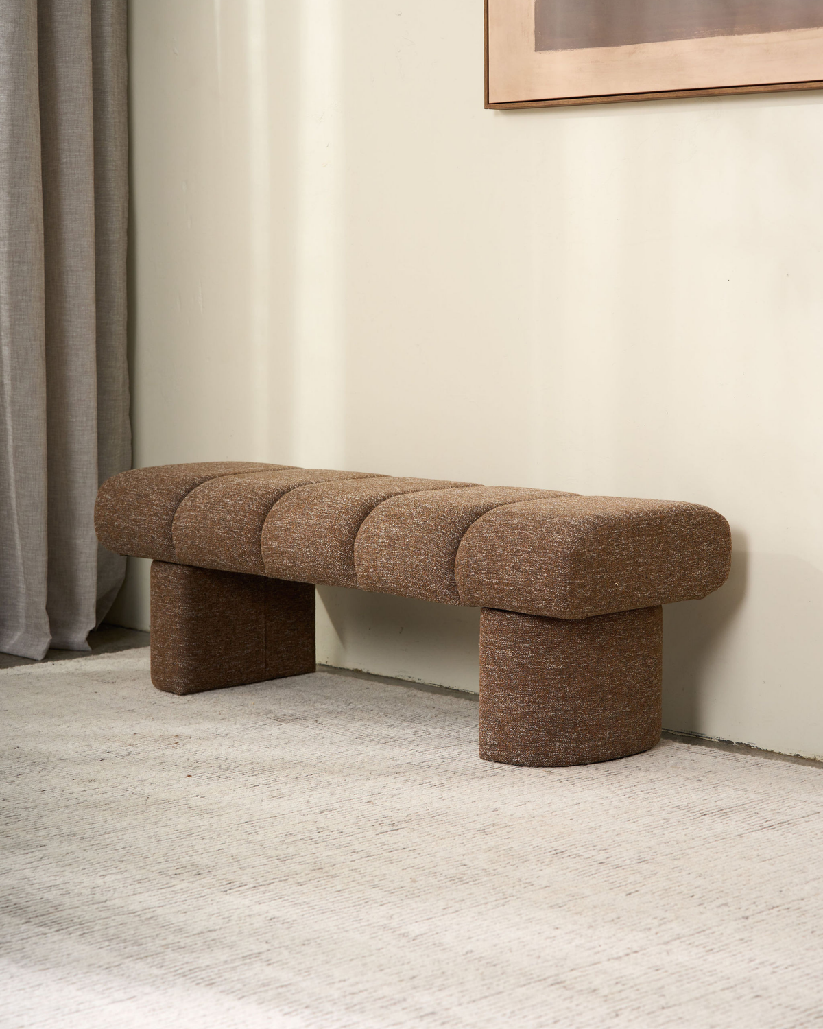 Lune Bench in Dusty Seed, flecked brown upholstery with pill-shaped legs, against a cream wall