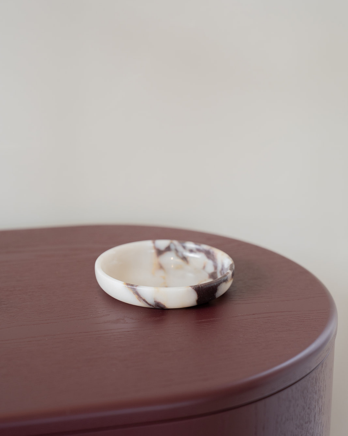 Empty Viola Marble Luvi Bowl on a deep burgundy timber side table against a pale wall