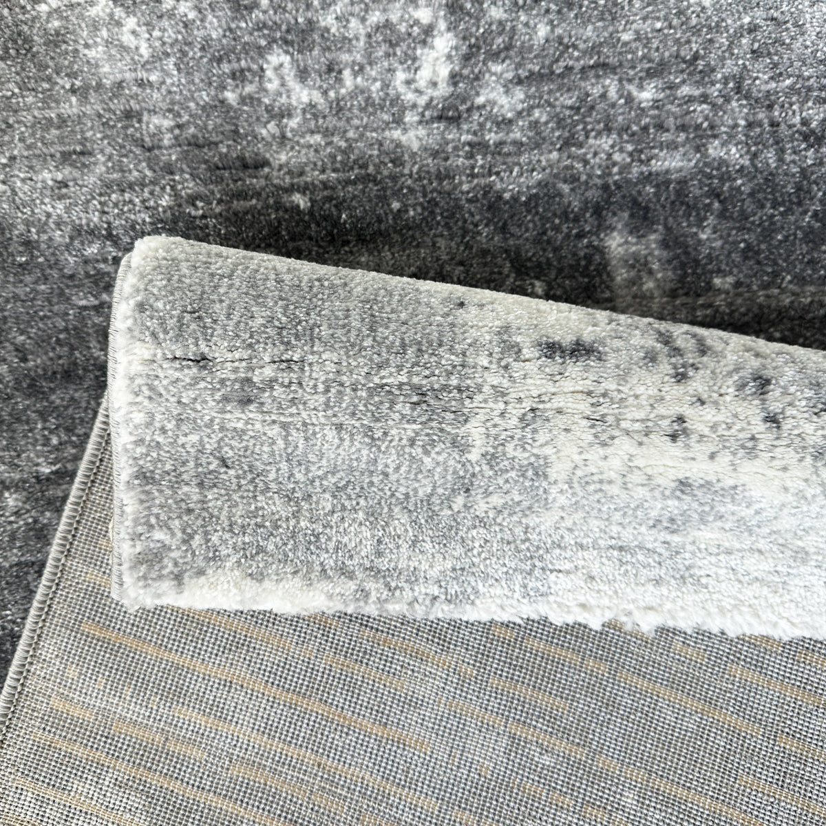 Grey abstract rug folded back to show the woven backing