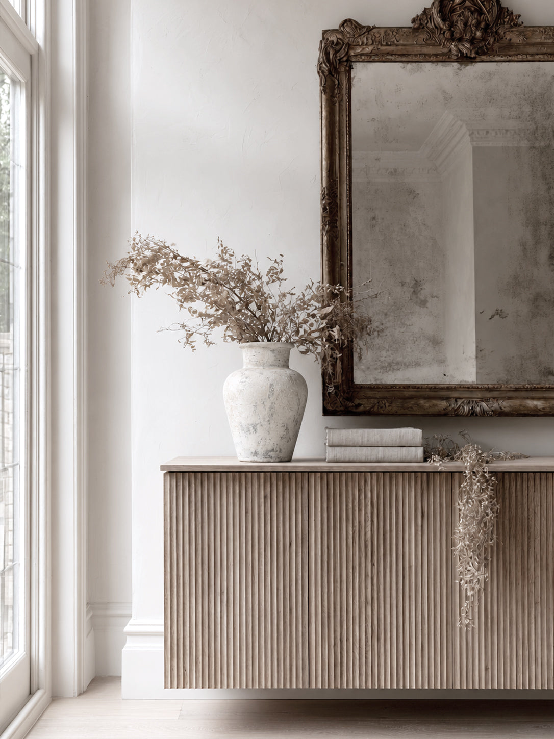 Mariella 40cm distressed stone terracotta vase with dried botanical branches styled on fluted oak sideboard beneath ornate antiqued mirror