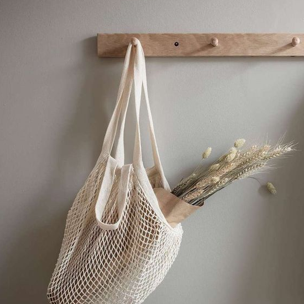 Cream string market bag hanging from a wooden peg rail with dried grasses inside