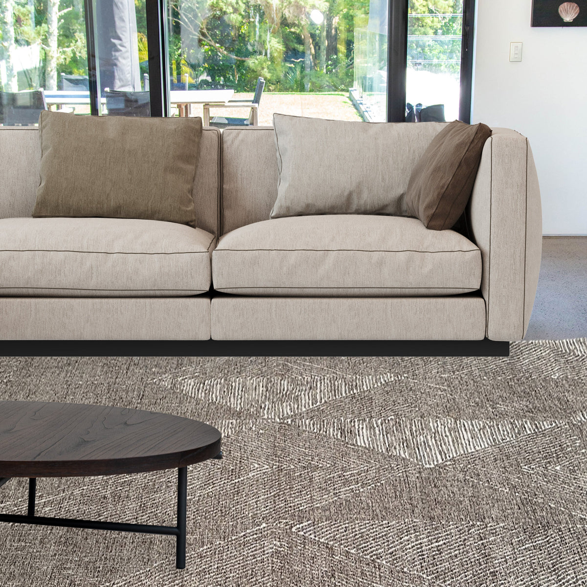 Brown chenille rug under a round black coffee table in front of a taupe sofa and garden windows