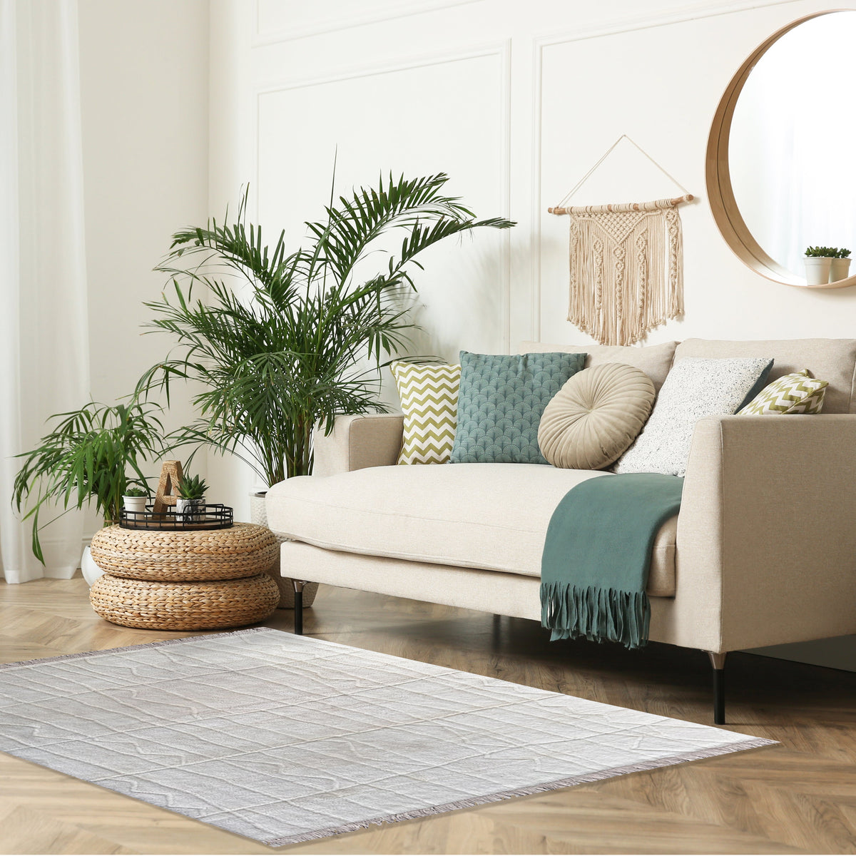 Ivory textured rug in front of a cream sofa with a teal throw, potted palm, round mirror and woven pouf