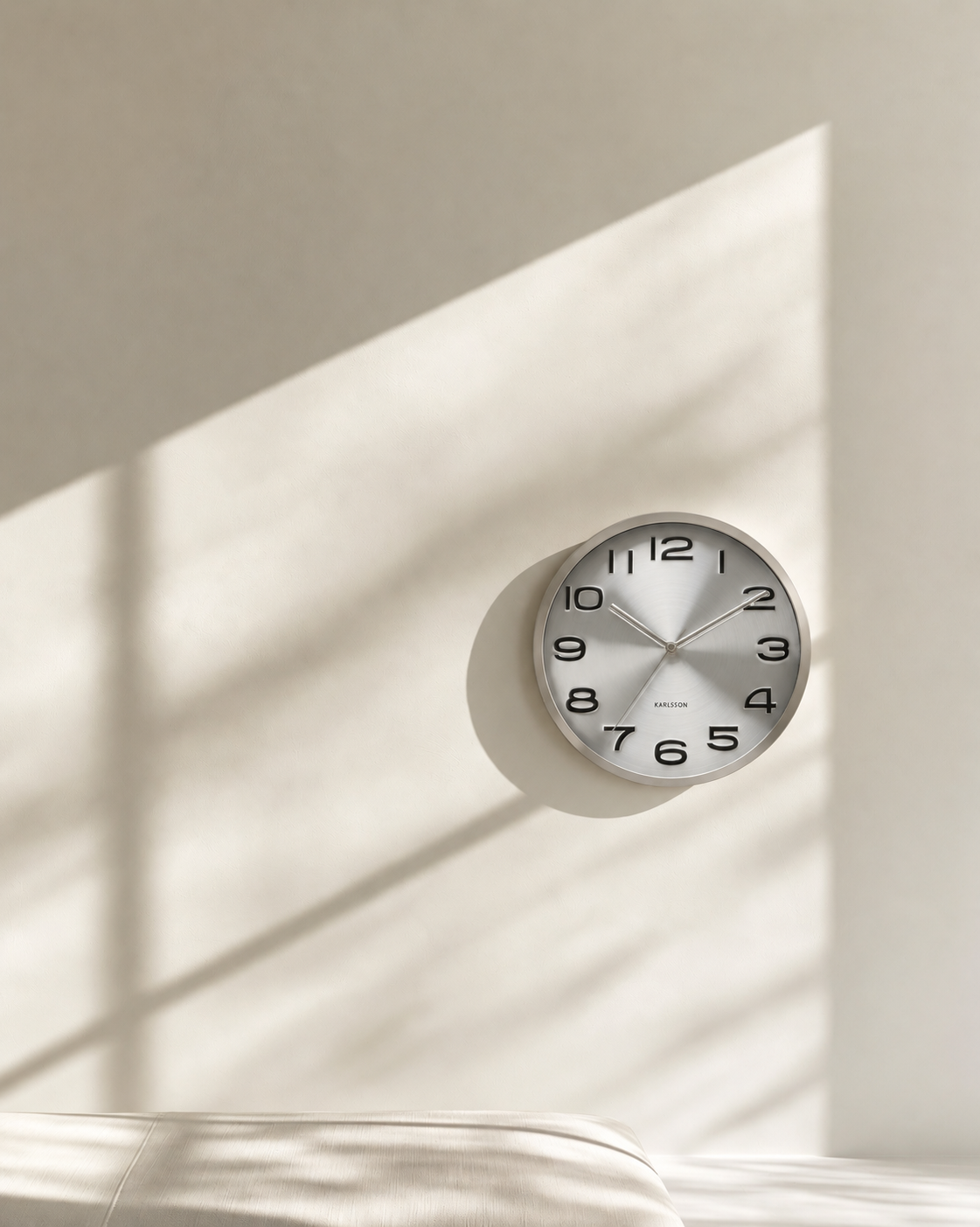 Maxie Wall Clock in brushed steel on a warm white wall in soft afternoon light
