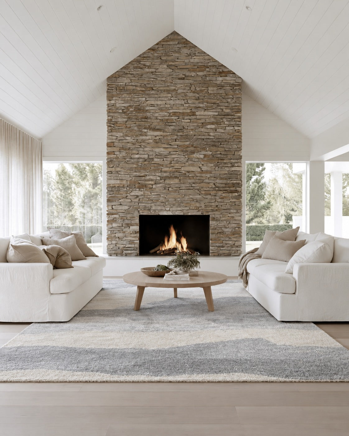 Mercer Cloud Grey Rug between two white sofas under a round timber coffee table, in a vaulted lounge with a stone fireplace