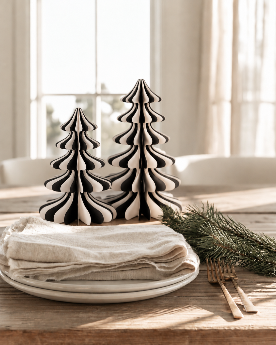 Monochrome honeycomb paper trees in 20.5cm and 25cm on a timber dining table beside stacked plates, linen napkin and pine