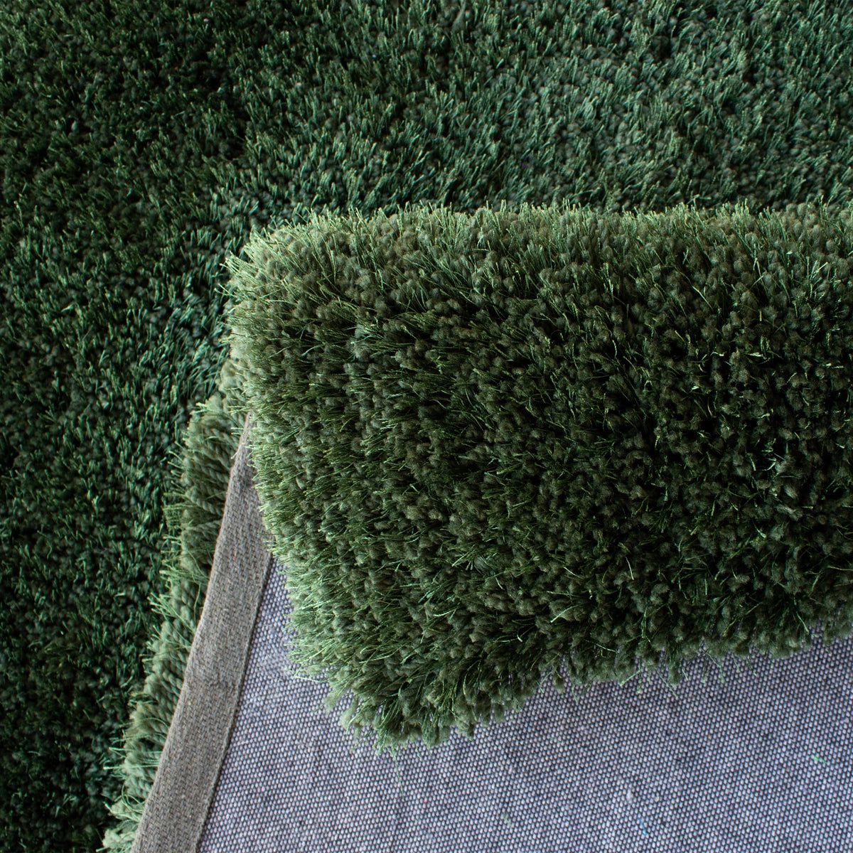 Folded edge of the forest green rug showing the pile depth and grey backing