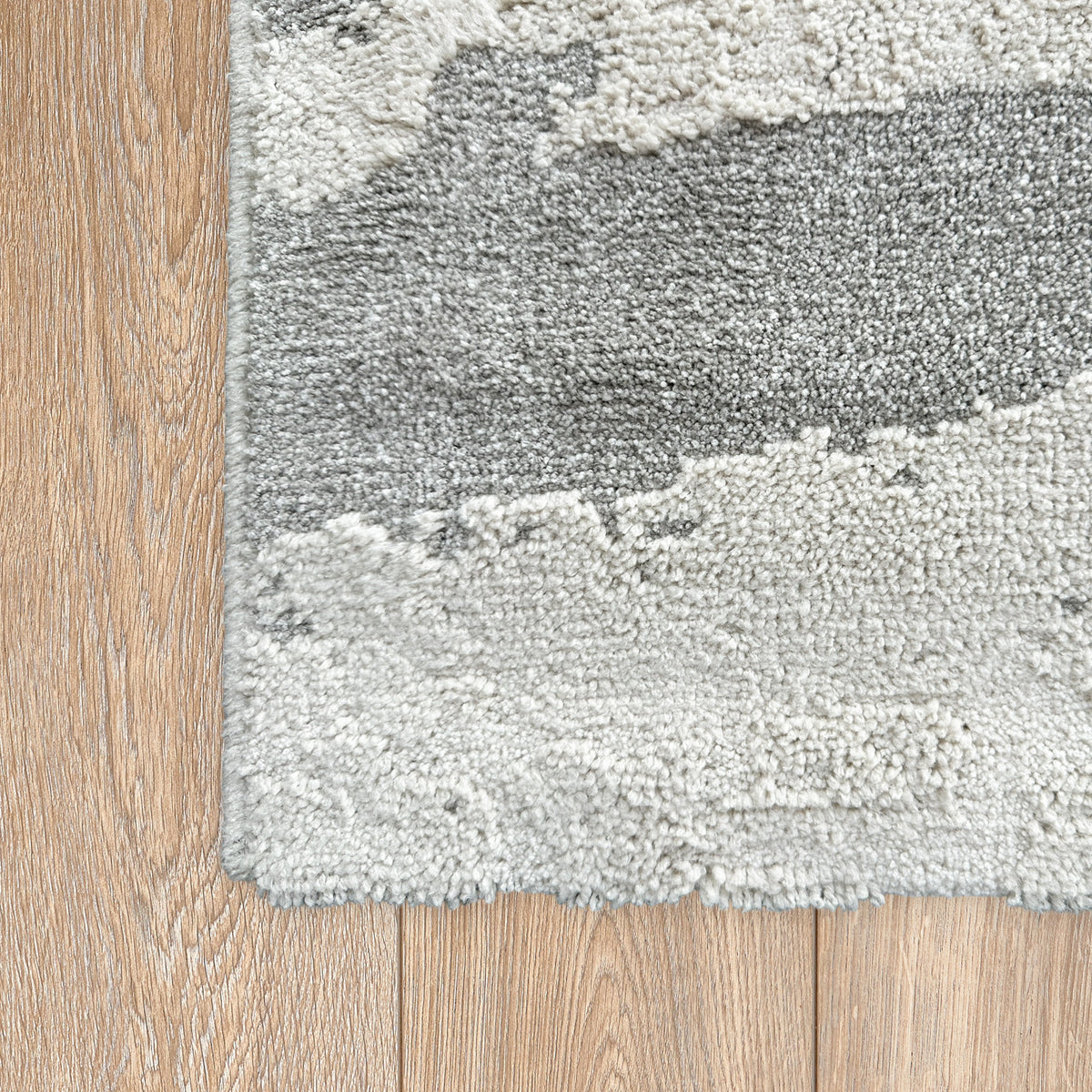 Corner of the grey and beige abstract rug on a light timber floor