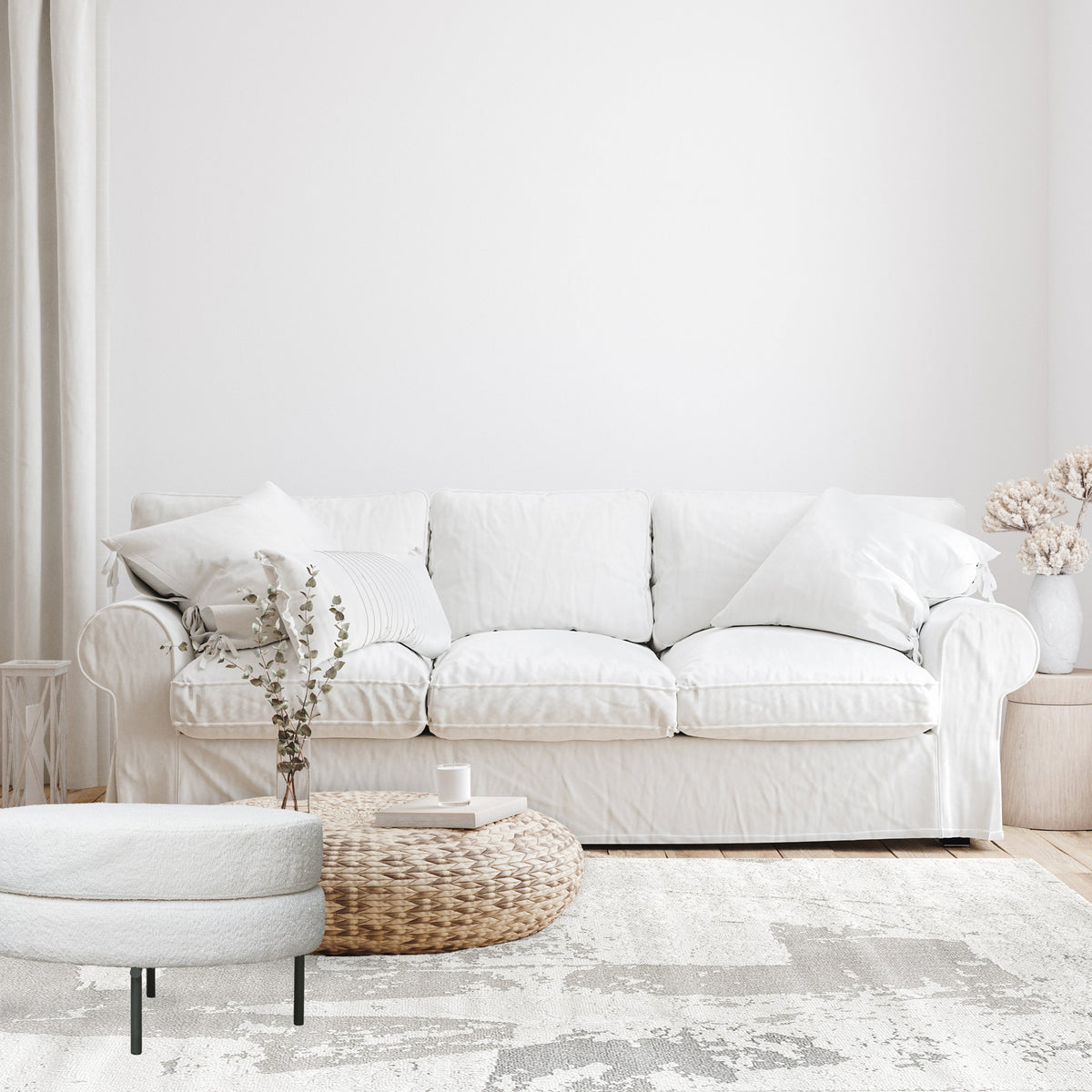Grey and beige abstract rug in a white lounge with a slipcover sofa, round ottoman and woven basket