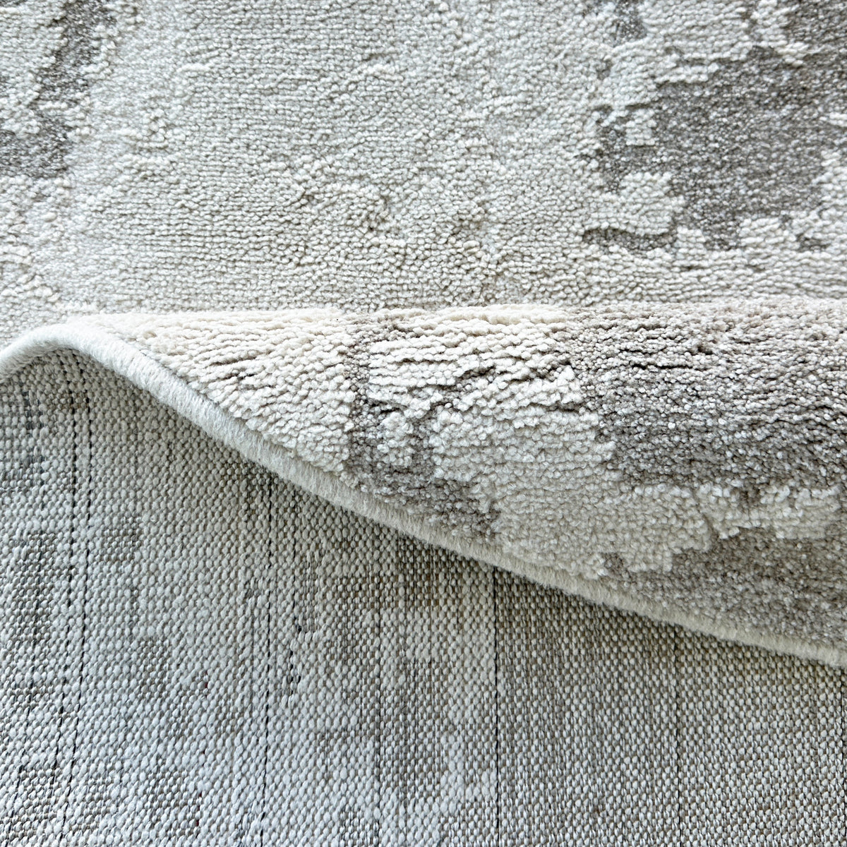 Edge of the round grey and beige rug folded to show the backing