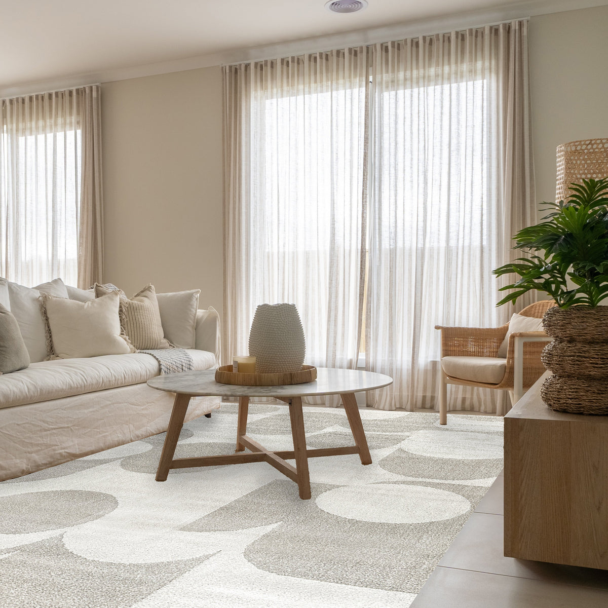 Beige geometric rug in a bright lounge with a cream sofa, round timber coffee table and sheer curtains