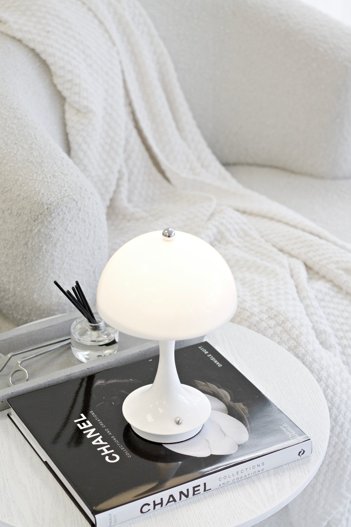 White mushroom lamp lit on stacked monochrome books beside a reed diffuser and a cream throw