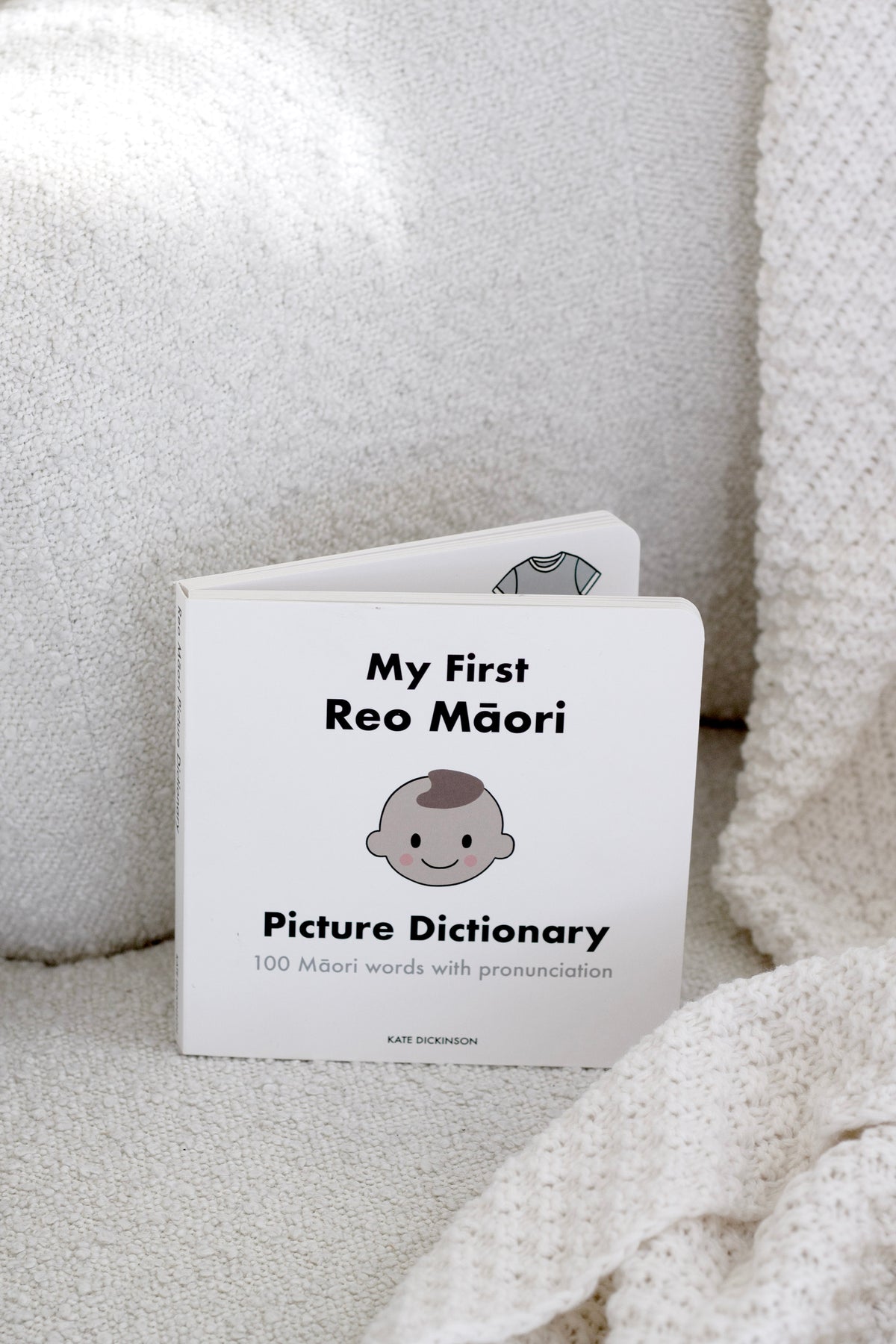 My First Reo Māori Picture Dictionary board book styled on a soft cream armchair with a knitted throw.