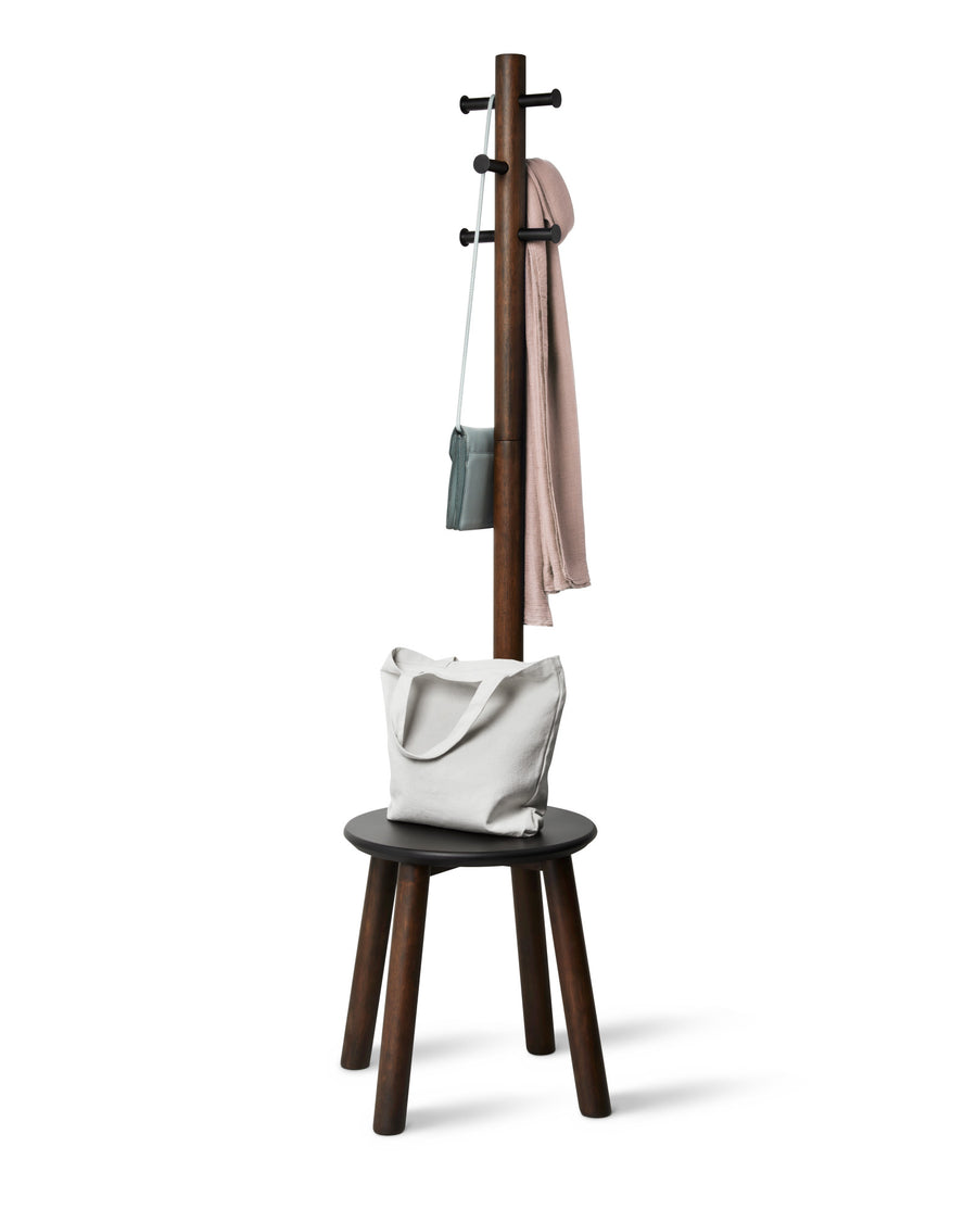 Umbra Pillar stool and coat rack in black and walnut holding a coat, bag and tote