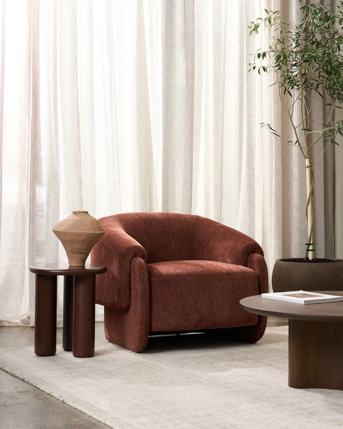 Living room with the Umber chair, a dark pill-leg side table, olive tree and round coffee table