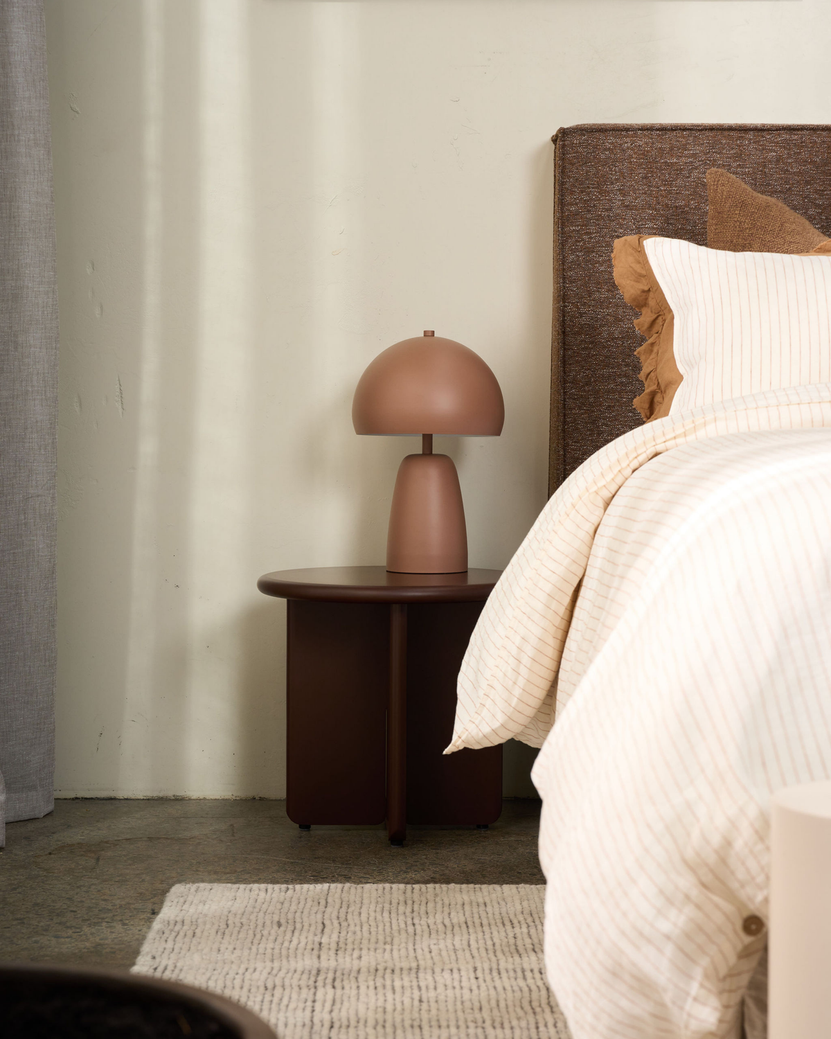 Cross-base side table in a dark brown finish used as a bedside with a terracotta mushroom lamp