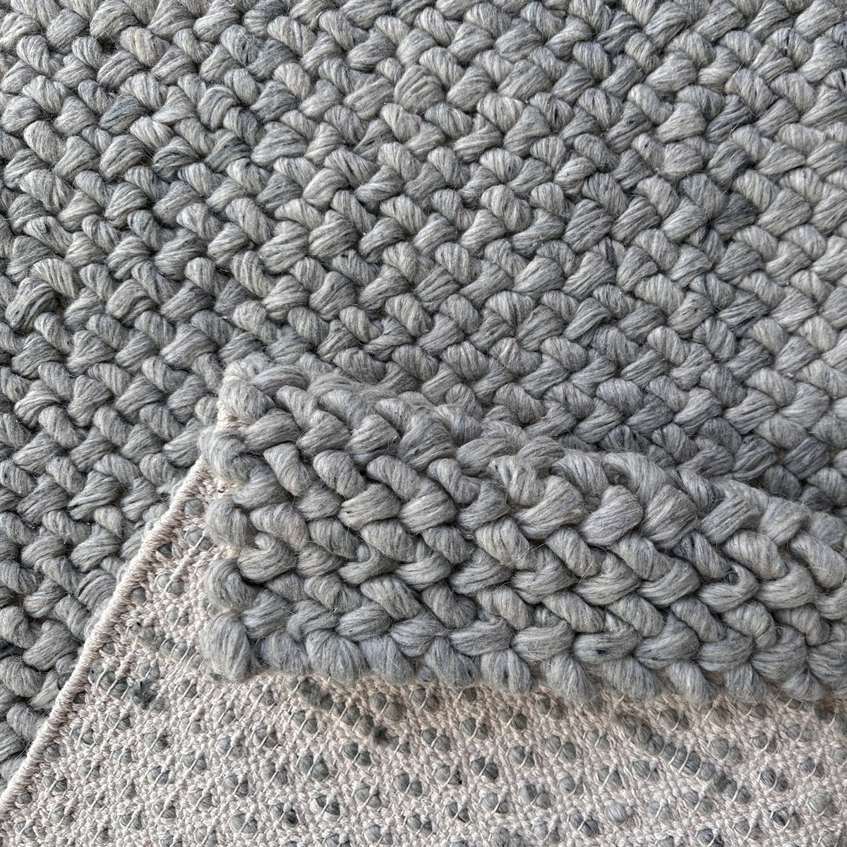 Folded corner of the grey braided rug showing the pale backing