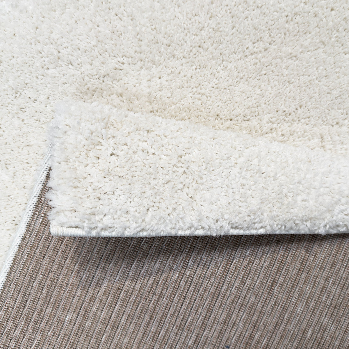 Folded corner showing the white plush pile and the woven grey backing