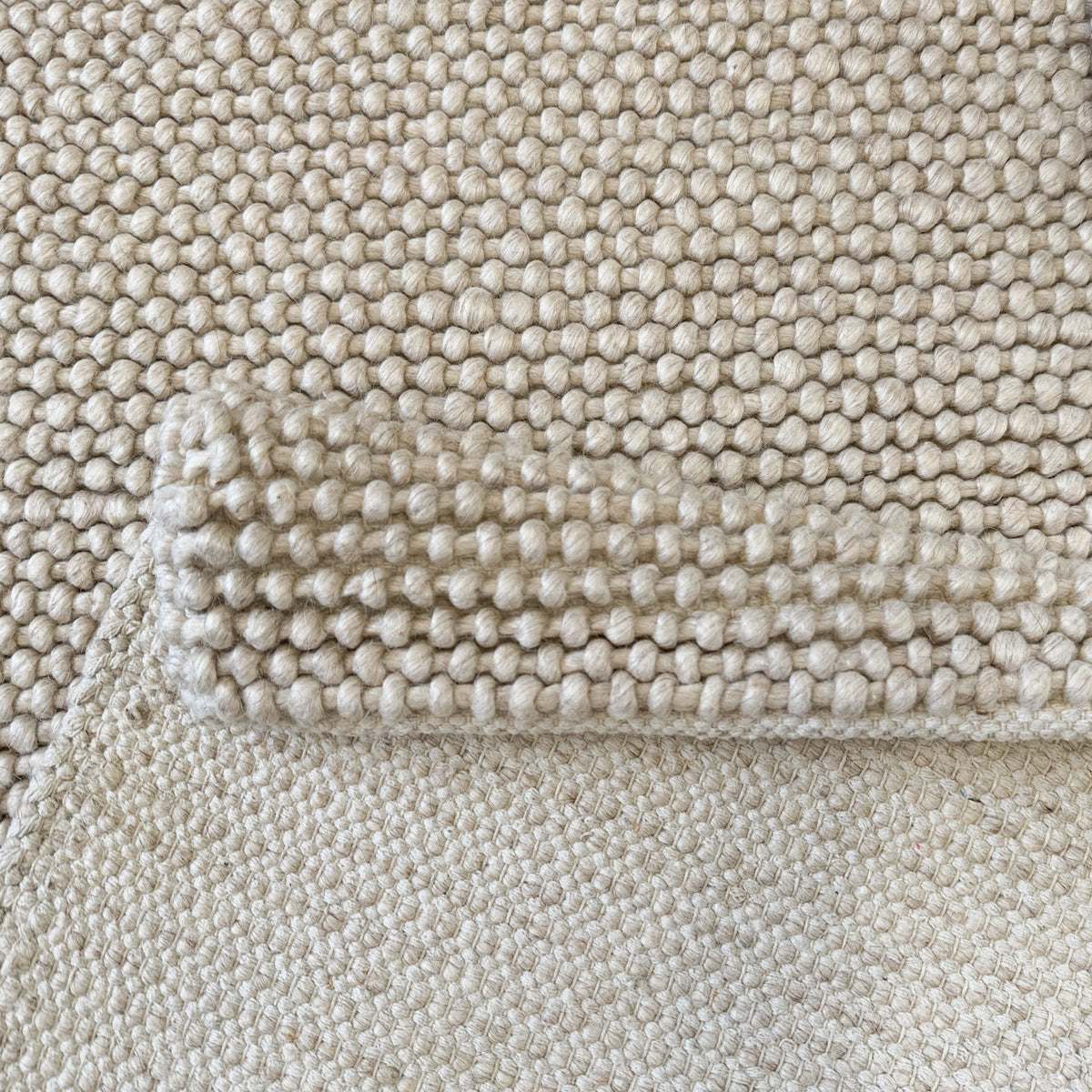 Folded edge of the beige rug showing the loop weave and its underside