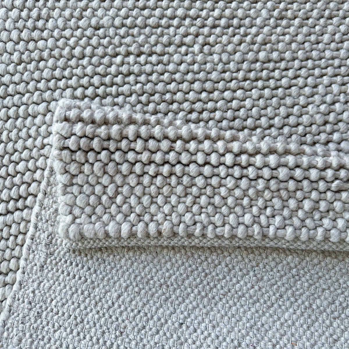 Folded edge of the grey rug showing the loop pile and the reverse