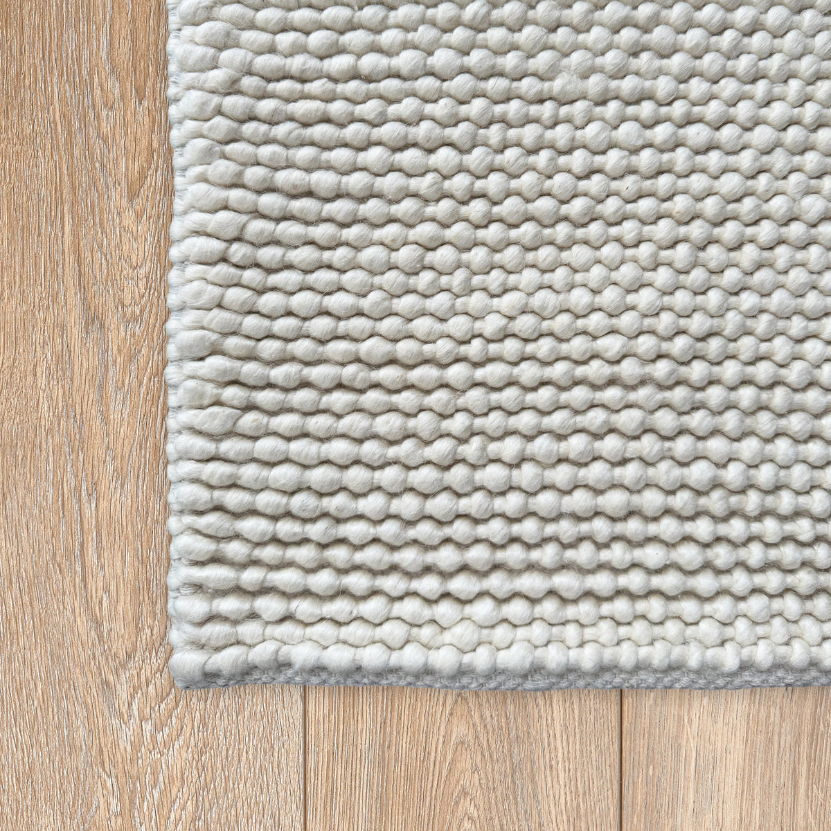 Corner of the ivory loop rug on a pale timber floor showing the bound edge