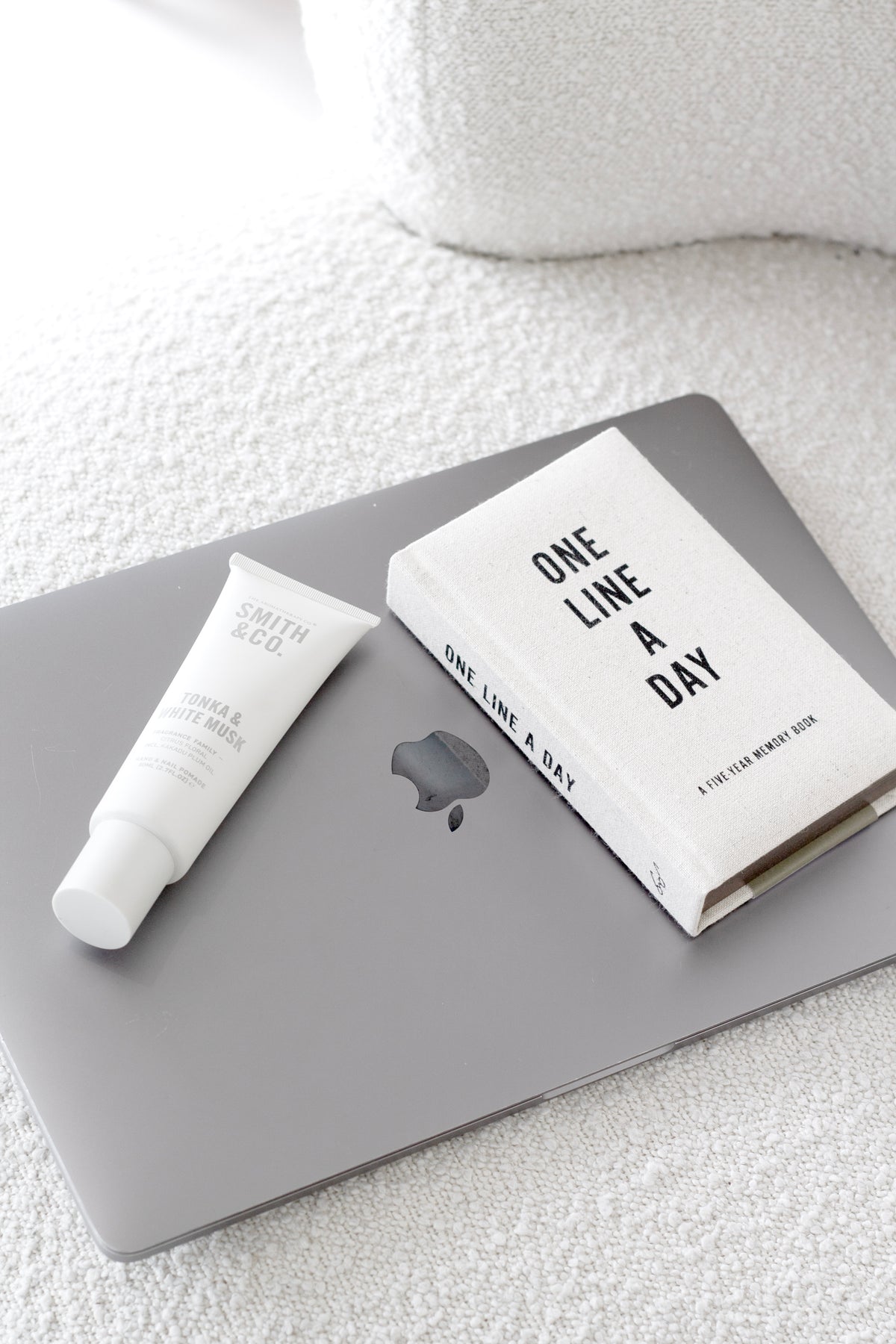 Flatlay of the One Line a Day journal on textured fabric with a laptop and hand cream
