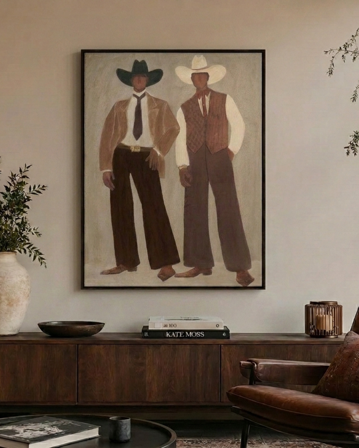 Outlaws Print above a dark timber sideboard with a carved bowl, stacked books, candle lantern and leather armchair
