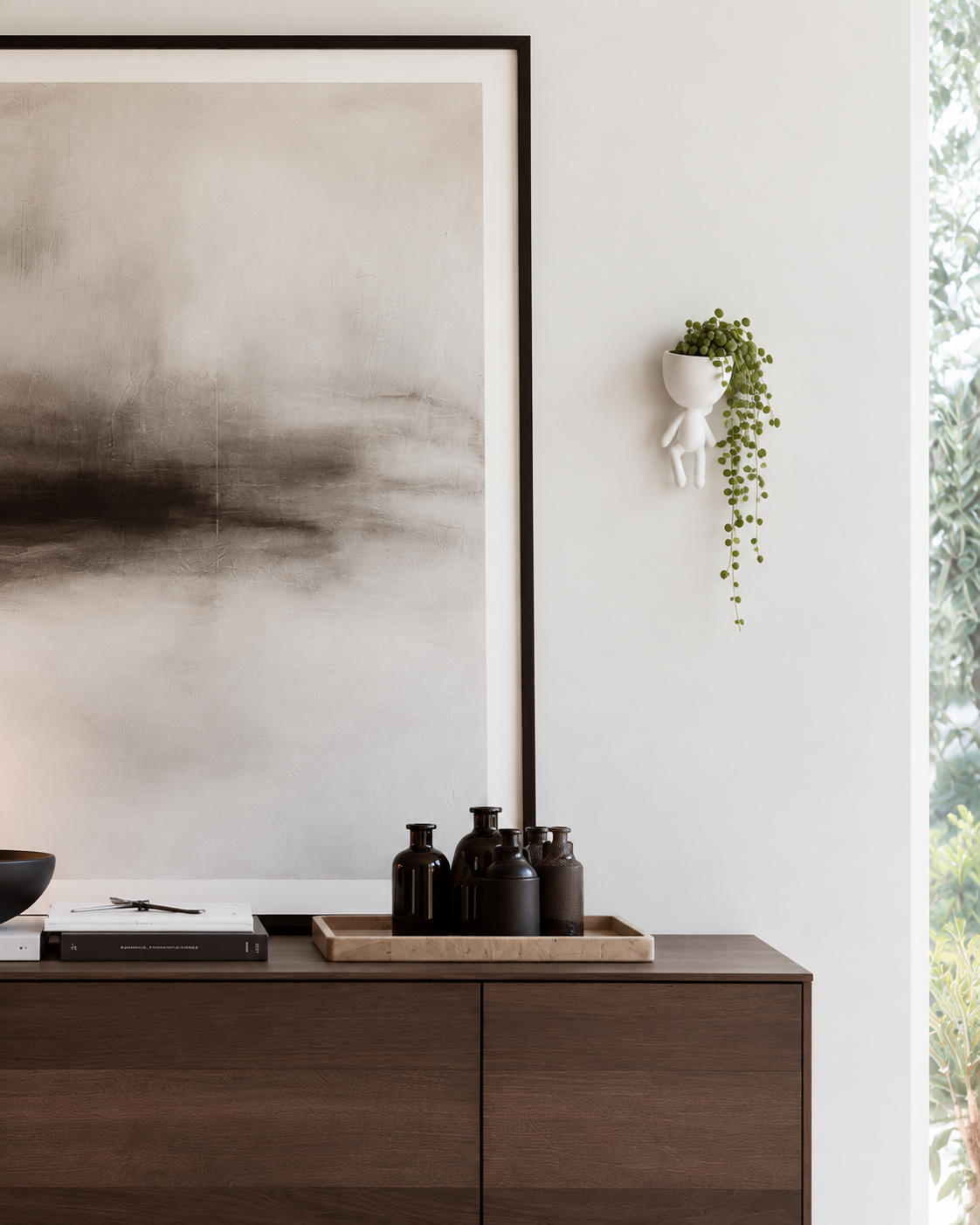 White figure wall planter with string of pearls above a walnut sideboard and abstract artwork