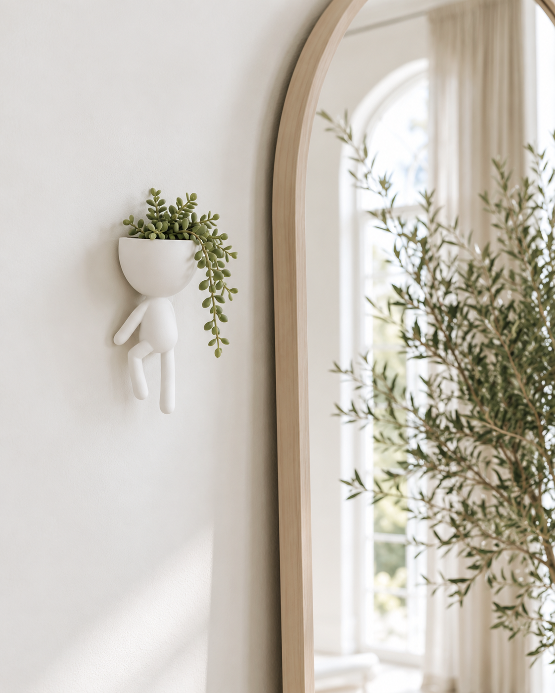 White figure wall planter with trailing succulent hung beside an arched oak mirror