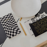 A limited edition THE CHECKLIST NOTEBOOK BLACK from Papier HQ on a table next to a gold pen.