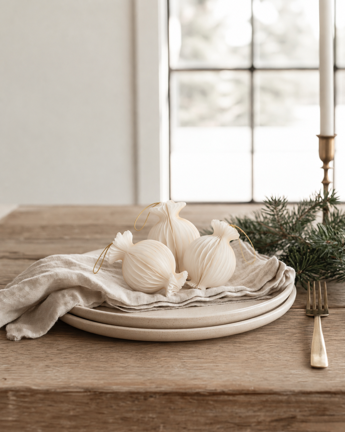 Three gilded lolly hanging decorations in off white with gold loops, on stoneware plates with a linen napkin