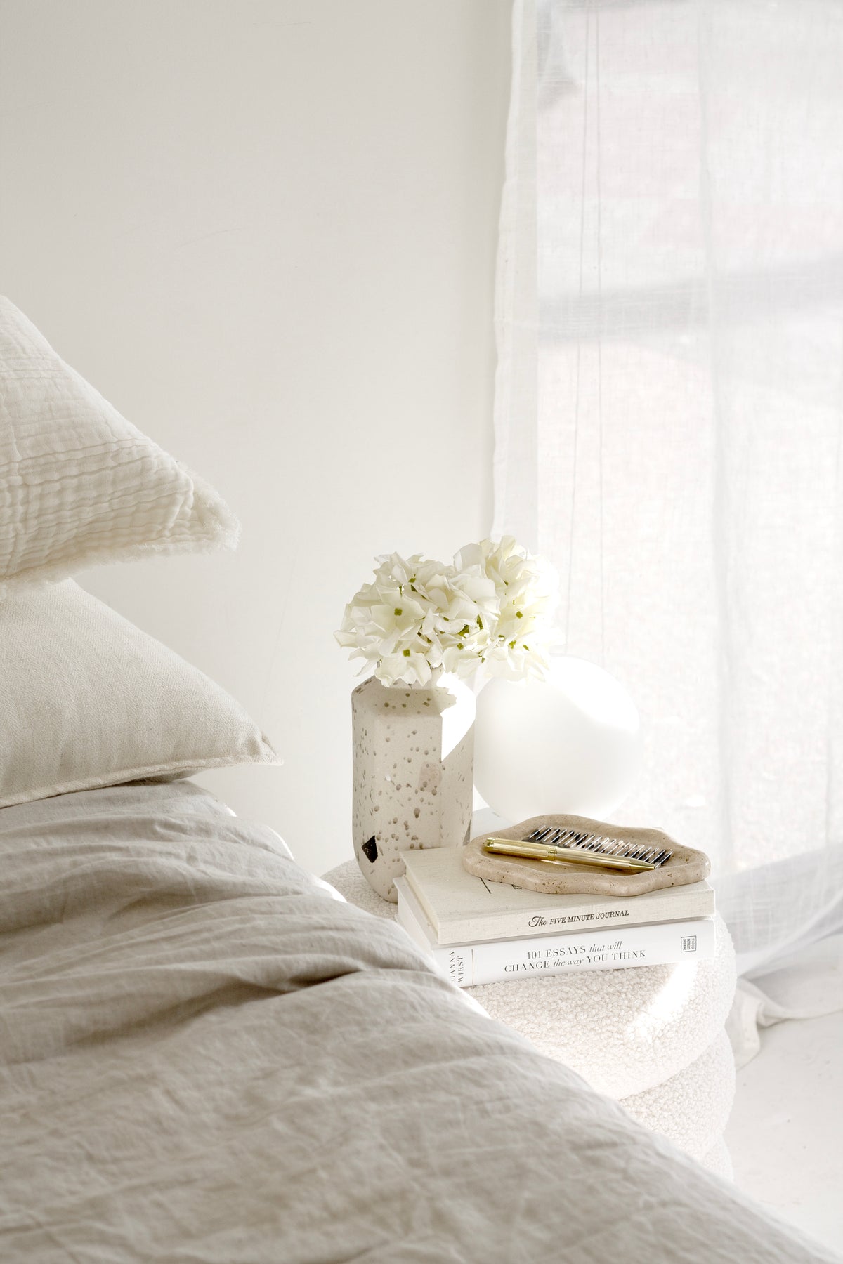 Petite white hydrangea faux stem in ceramic vase on neutral bedside table