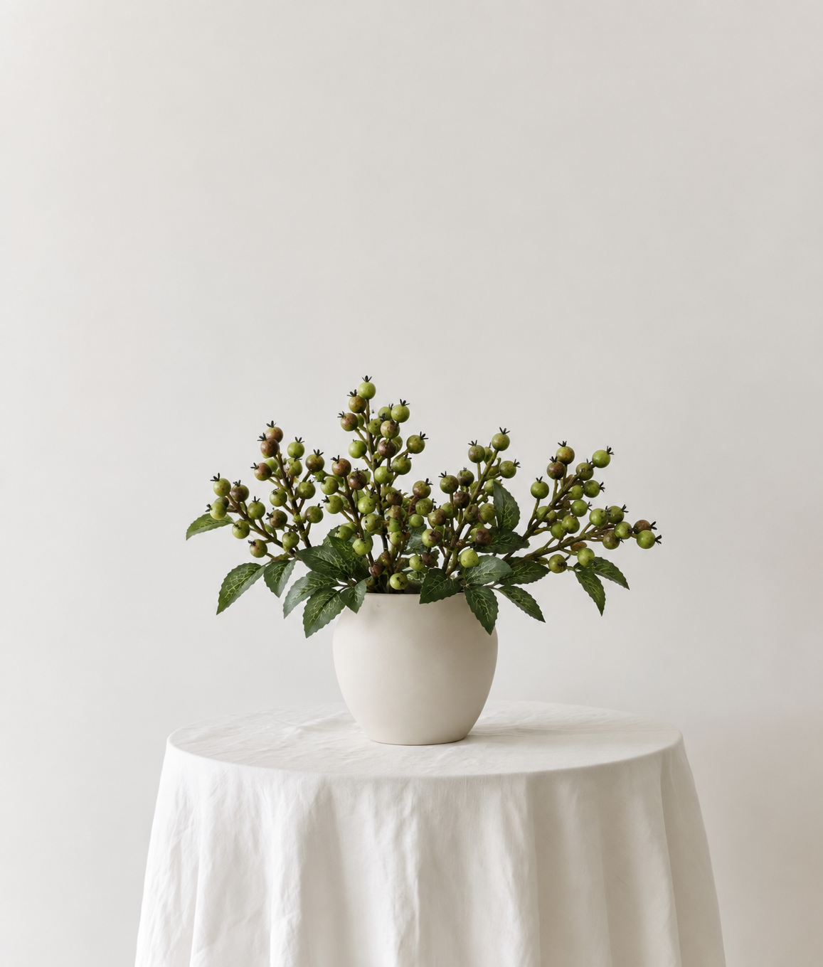 Rattan Berry Stems in spiced green in a cream ceramic pot on a linen-draped side table