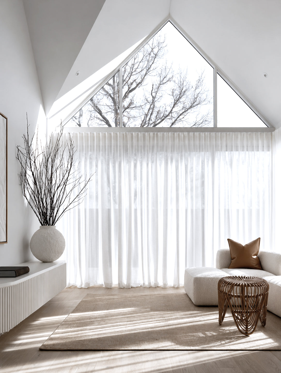 Rattan tulip stool in a bright room with a gabled window and sheer linen curtains