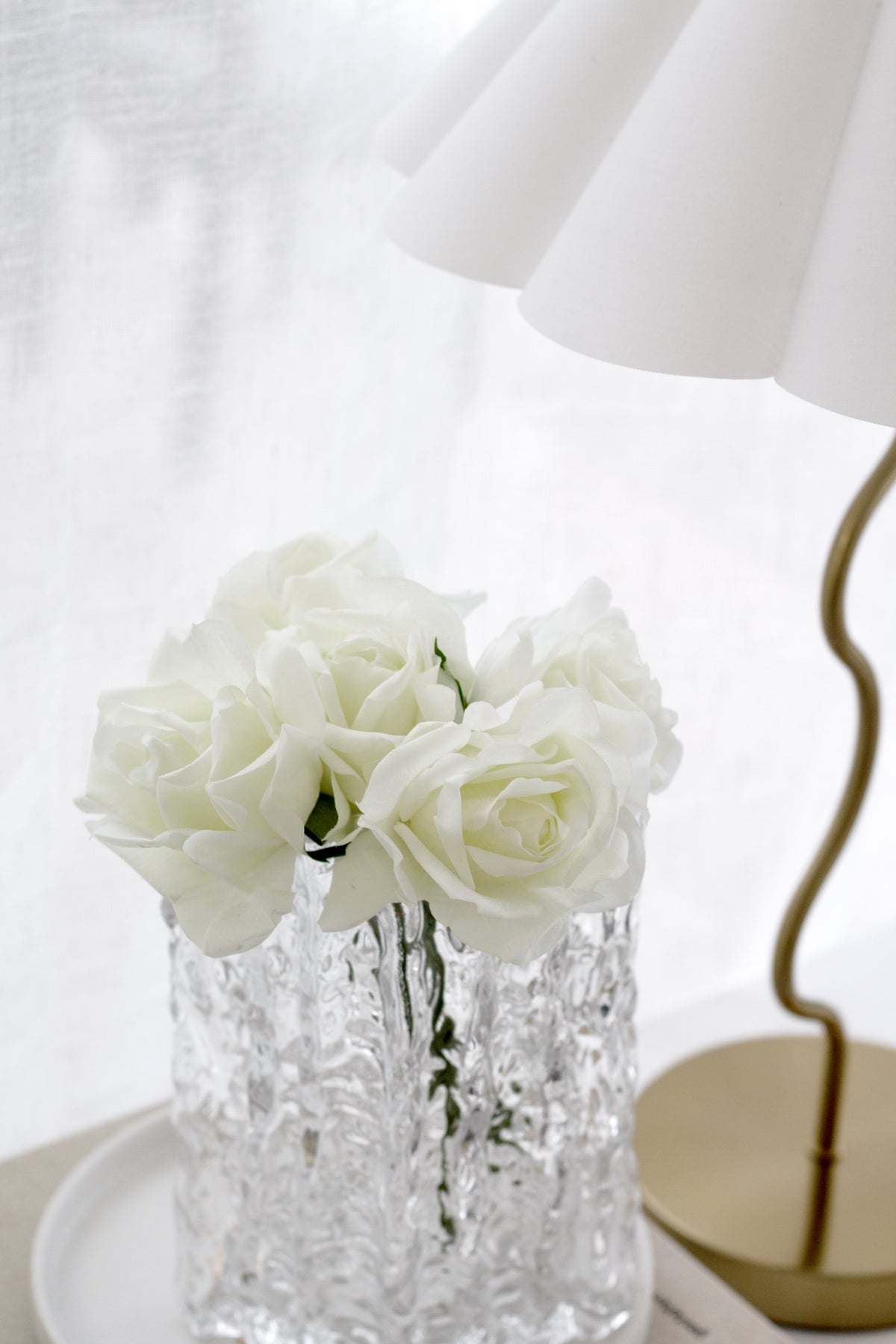 Real Touch Rose Bundle of white artificial roses styled in a textured glass vase beside a gold lamp.
