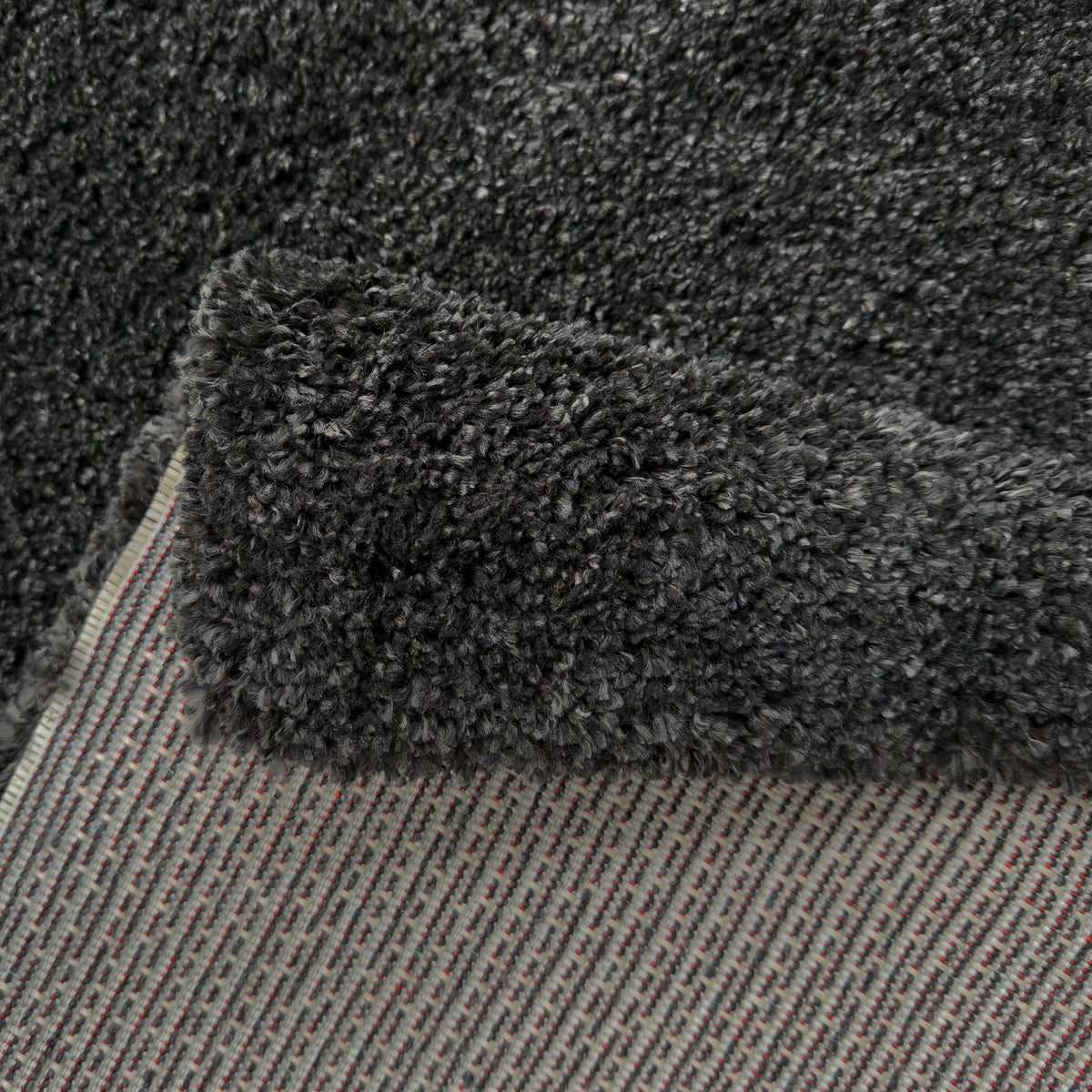 Folded corner of the charcoal rug showing the woven backing