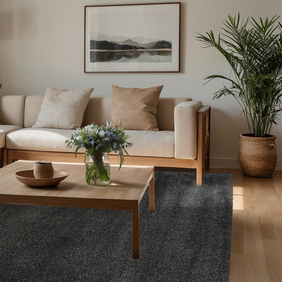 Charcoal rug under a timber coffee table in front of a linen sofa with a potted palm