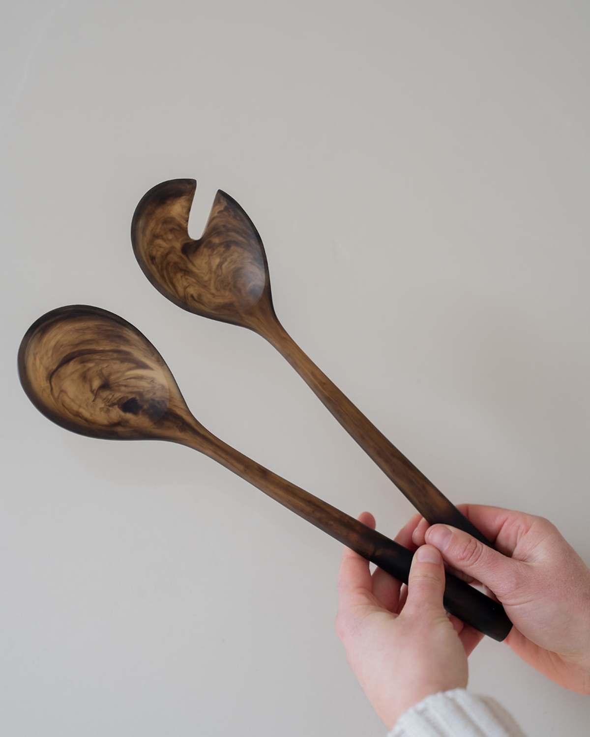 Hand holding the Chocolate resin salad servers upright against a pale wall