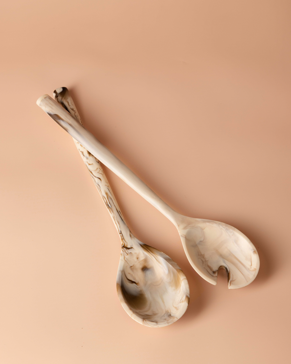 Tiramisu resin salad servers crossed on a peach background, cream resin with caramel marbling