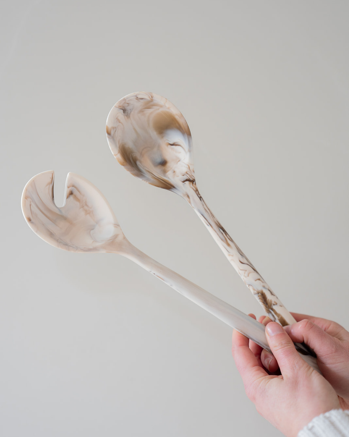 Hand holding Tiramisu resin salad servers, showing the slotted fork tip and long marbled handles