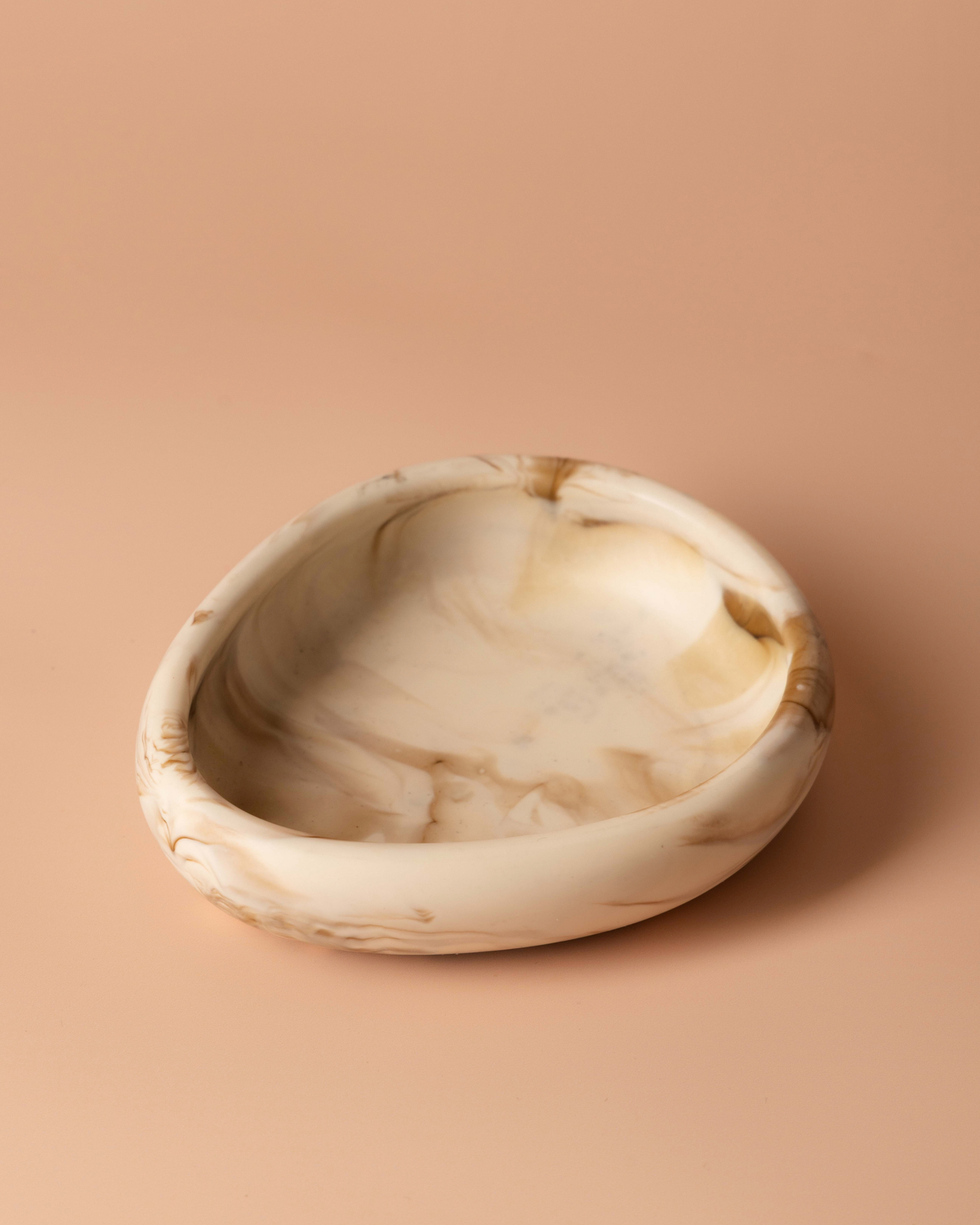 Tiramisu small bowl on a peach background showing its rounded asymmetric rim and caramel swirls