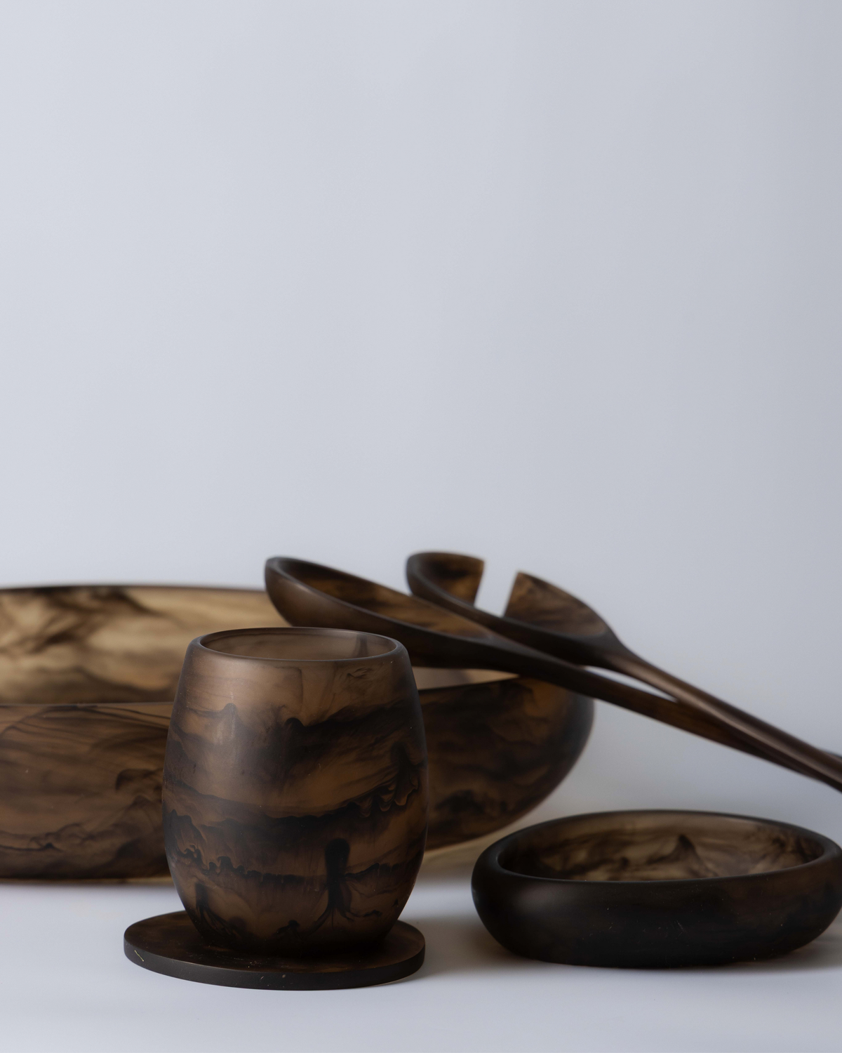 Chocolate tumbler on a resin coaster in front of matching salad servers, a small bowl and a large bowl