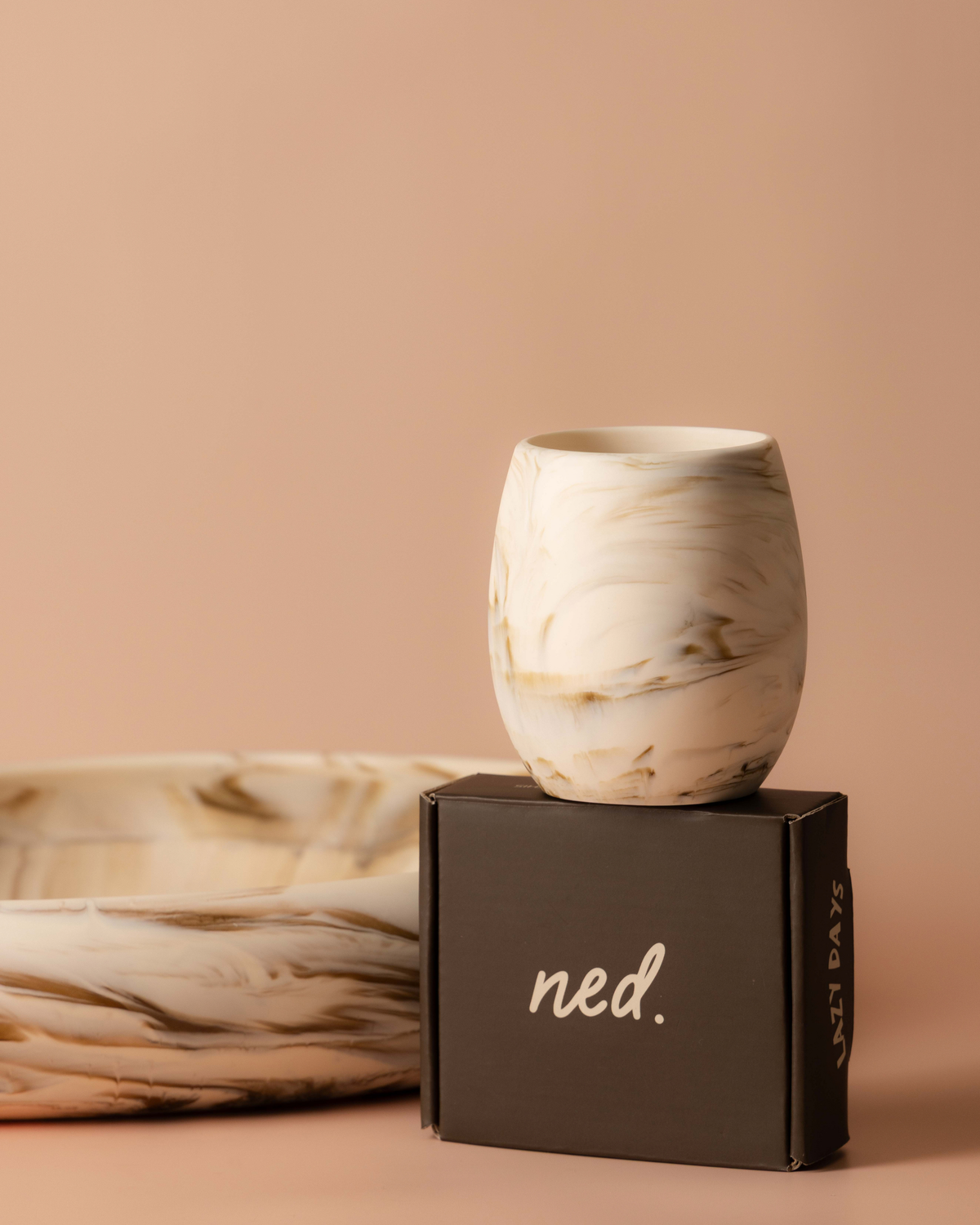 Tiramisu tumbler resting on a dark brown gift box beside a large cream marbled resin bowl