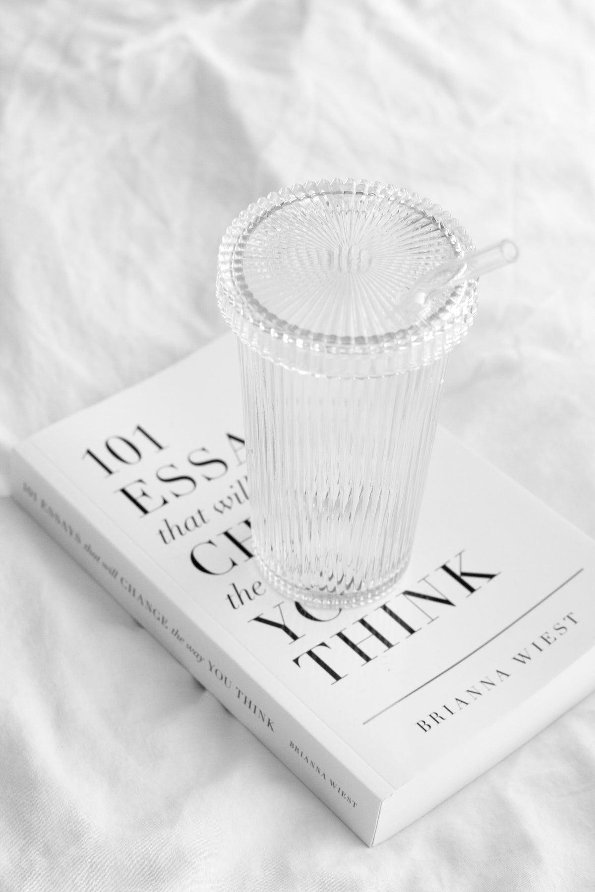 Ribbed glass tumbler with lid and glass straw styled on neutral book in soft light