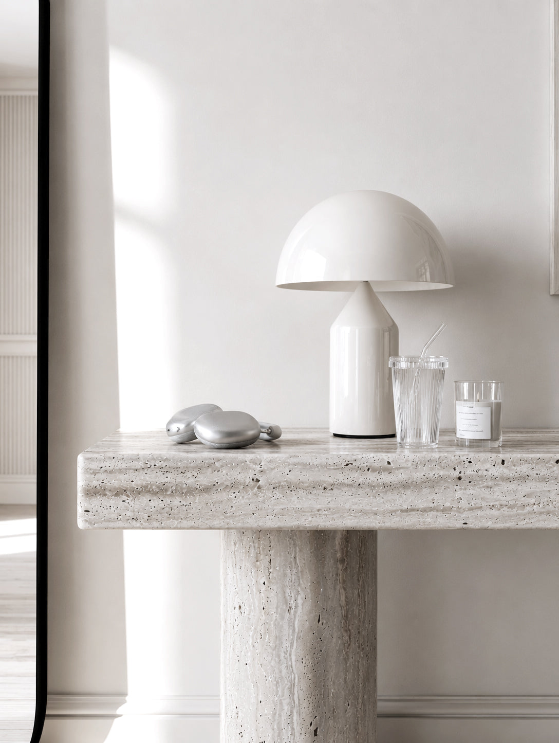 Ribbed glass tumbler with glass straw styled on travertine console with dome lamp and candle in minimal white interior