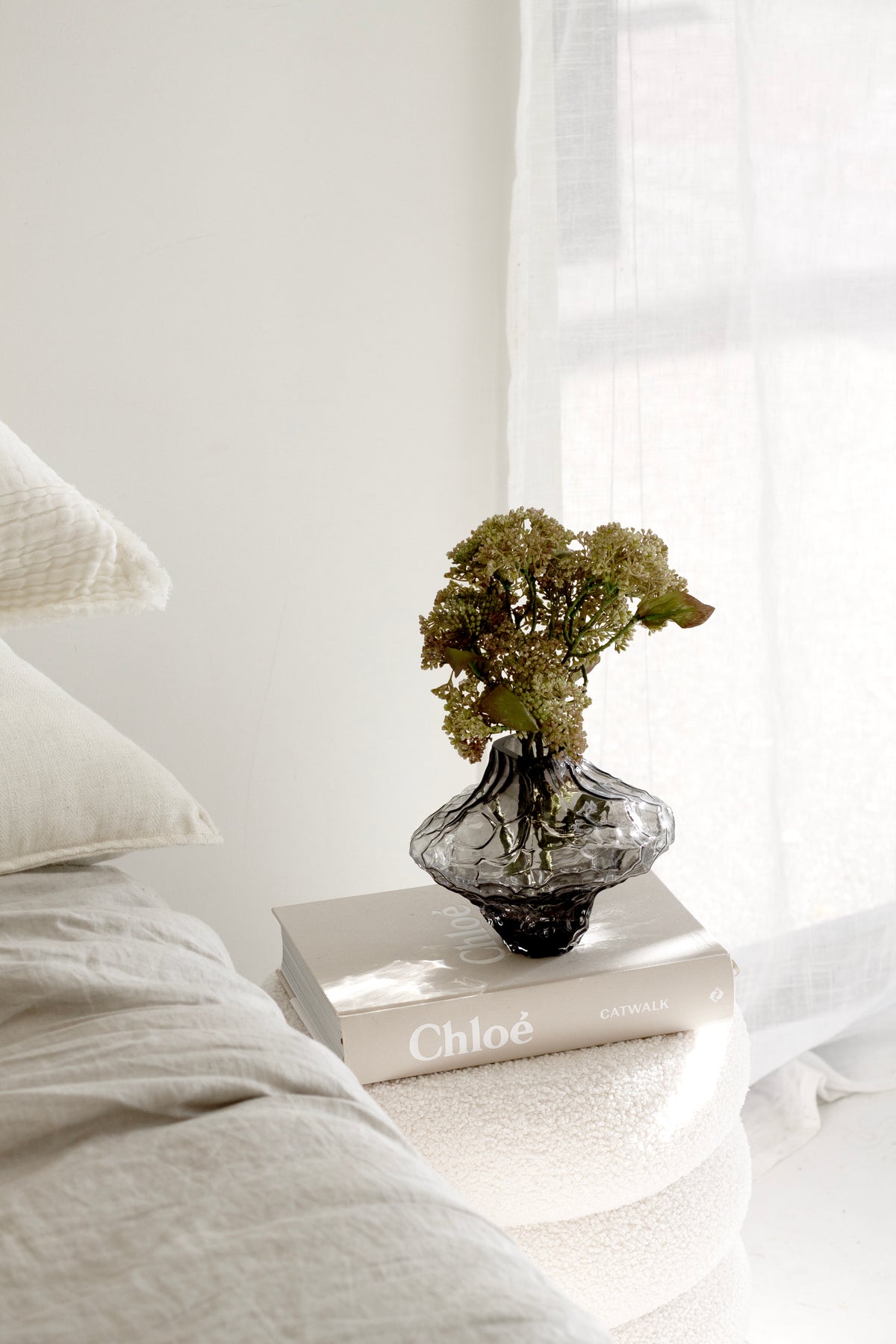 Smoky black rippled crystal glass vase with dried hydrangea on a book beside white bed linen