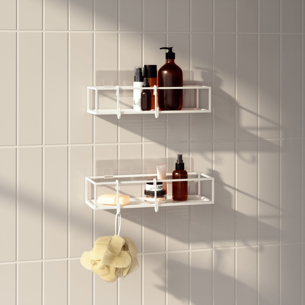 Two Umbra Cubiko shower bins in white on tiles, holding bottles with a loofah below